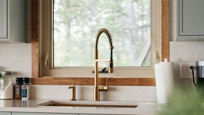 Une cuisine avec une fenêtre, un robinet doré et un porte-rouleau en papier.