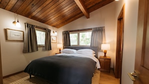 Une chambre avec un grand lit, des poutres apparentes en bois au plafond, deux lampes de chevet et une fenêtre avec des rideaux.