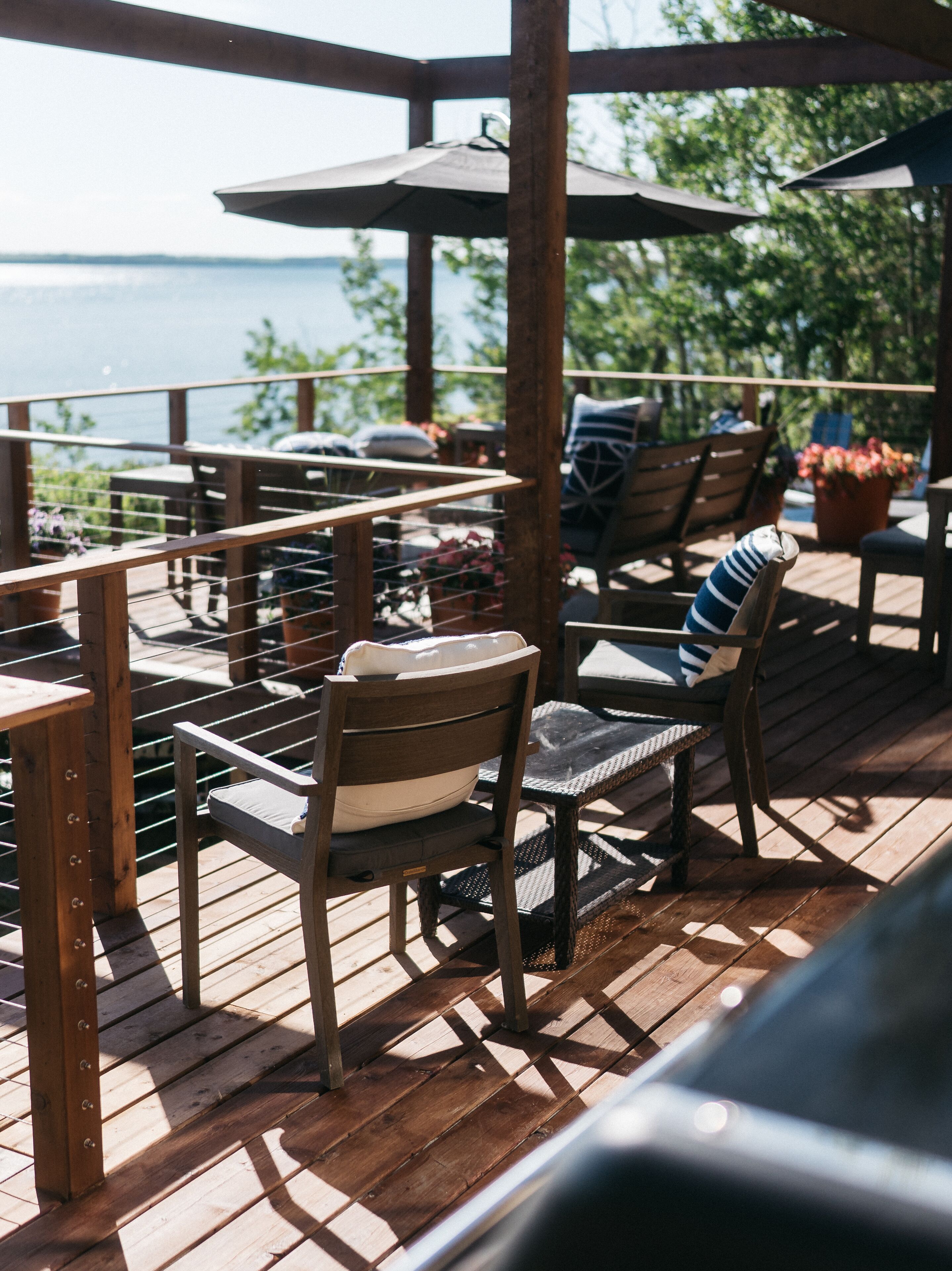 A wooden deck with outdoor furniture, including chairs and a table, overlooking a body of water.