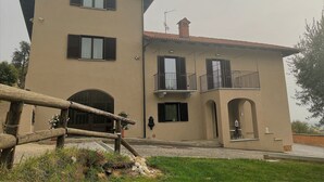 A two-story building with a beige facade, multiple windows with shutters, and a balcony with a railing.
