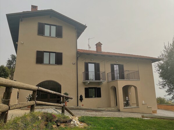 Un edificio de dos pisos con fachada color crema, varias ventanas con contraventanas y un balcón con barandilla.
