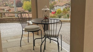 A patio with a round table and two chairs, a lantern, and a view of houses in the background.
