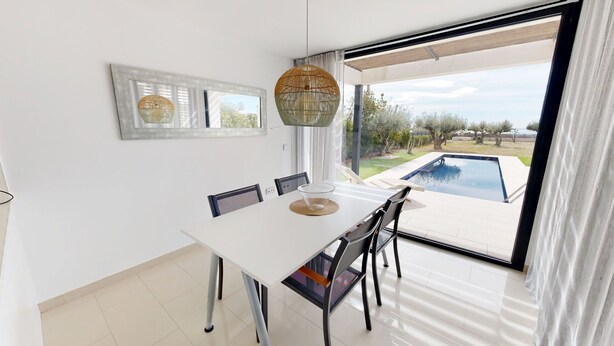 A dining area with a white table, chairs, and a view of a swimming pool. - Villa Lili (El Perelló)