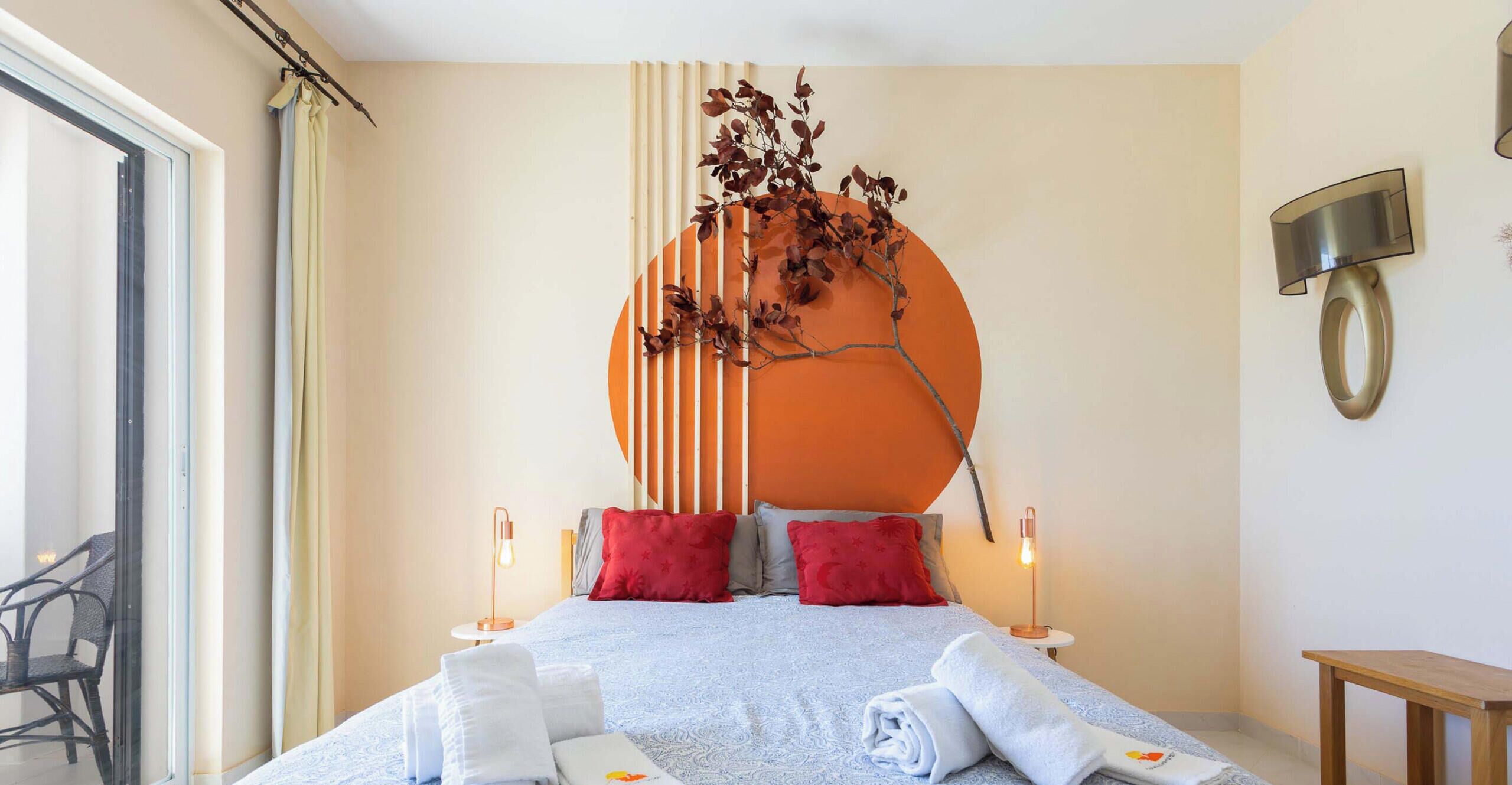 A hotel room with a bed, towels, a wall-mounted lamp, and a view of the outside.