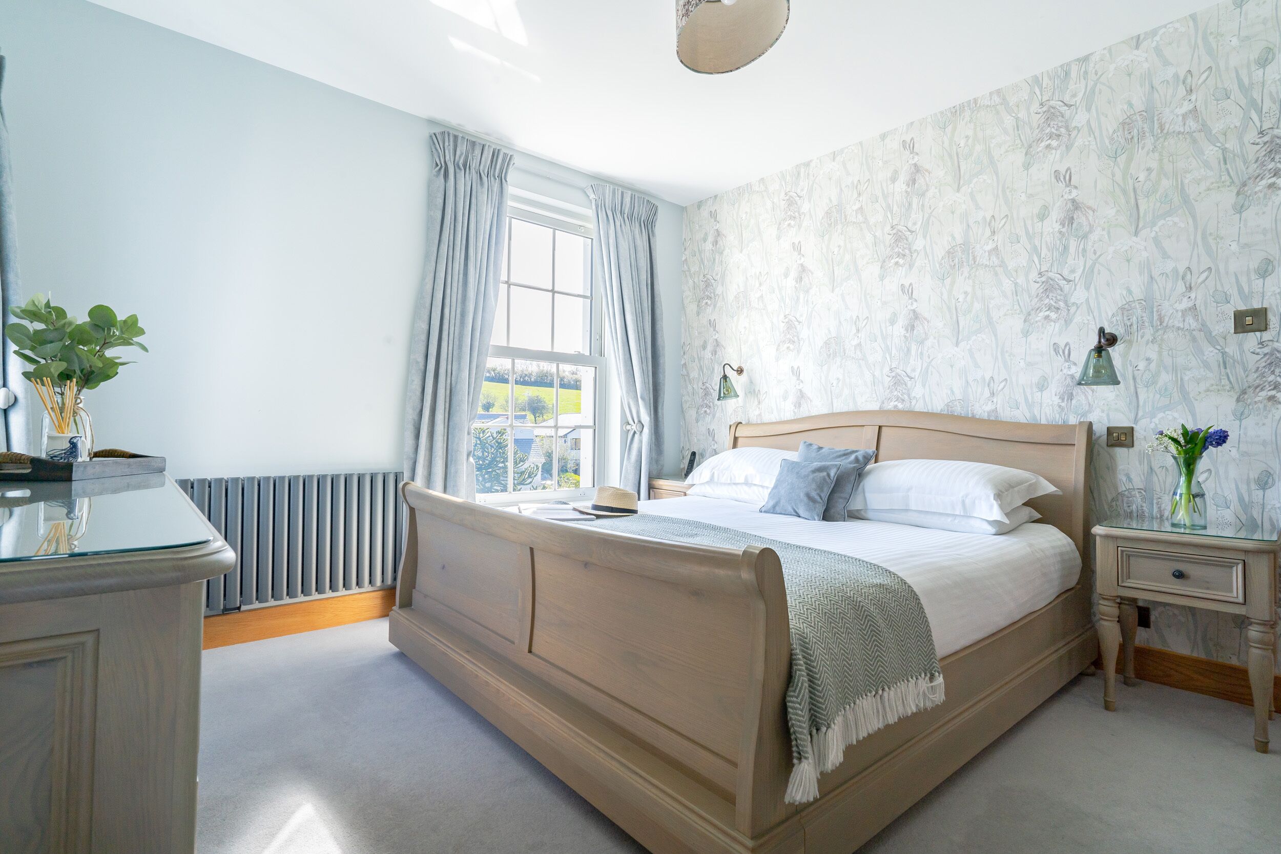 A bedroom with a wooden bed, a bedside table with a lamp, and a window with curtains.
