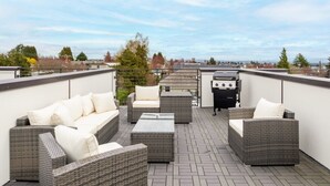A rooftop patio with wicker furniture, a grill, and a view of the cityscape.