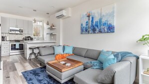 A modern living room with a grey sectional sofa, a wooden coffee table, and a cityscape painting on the wall.
