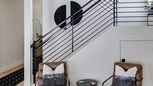Un intérieur moderne avec un escalier, deux fauteuils en cuir ornés de coussins à motifs et des œuvres d’art abstraites accrochées au mur.