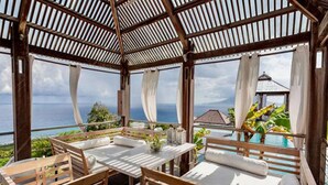 A wooden gazebo with a table and chairs, overlooking a pool and a scenic view.