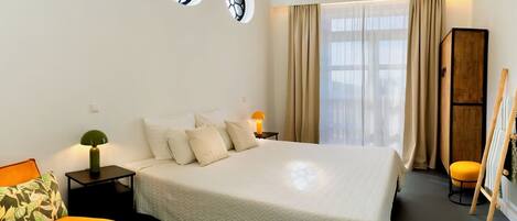 A hotel room with a bed, bedside tables, a lamp, a chair, a wardrobe, and a window with curtains.