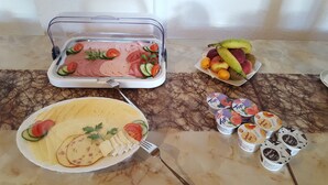 Een buffettafel met verschillende soorten eten, zoals vleesschotels, kazen, fruit en yoghurtbekers.