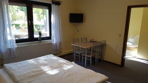 Een kamer met een bed, een tafel met stoelen, een televisie aan de muur en een raam met gordijnen.
