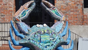 Eine Mosaik-Krabskulptur vor einem Backsteinhaus mit einer schwarzen Tür und Sterndekorationen.