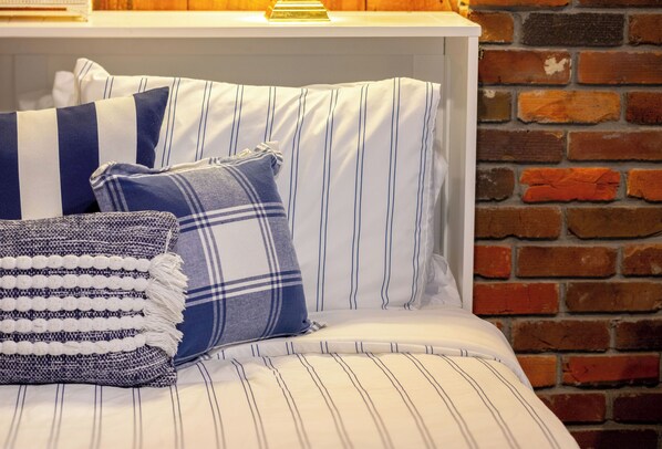 Una cama con ropa de cama a rayas y almohadas, una pared de ladrillo y un cabecero blanco.