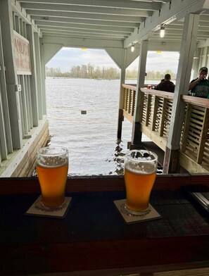 A covered outdoor seating area with two glasses of beer on coasters, overlooking a body of water. - Newly renovated cottage close to waterfront and boat ramps (Washington)