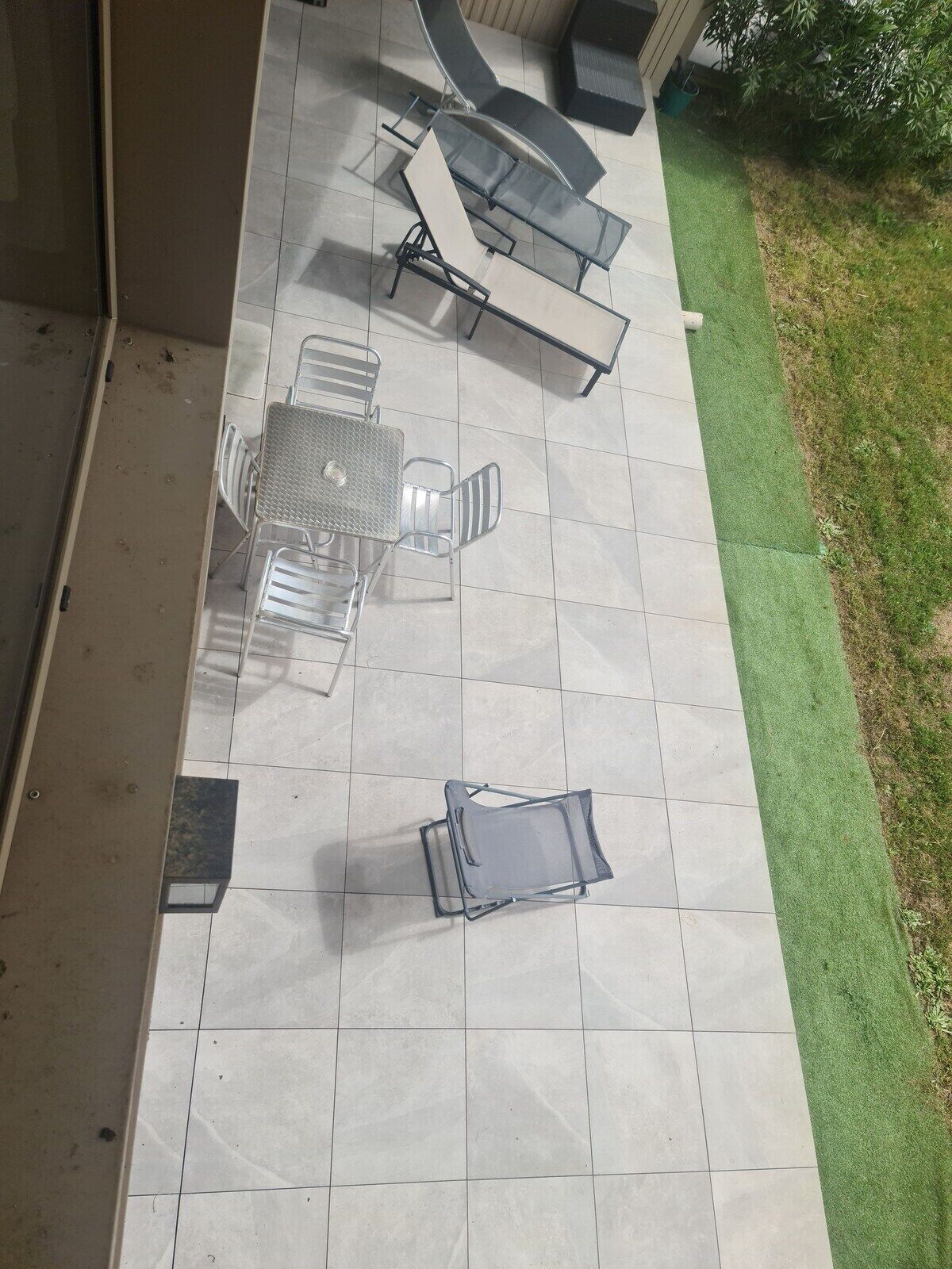 A patio with a glass-top table and chairs, a small table with chairs, and a folding chair.