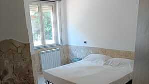 A bedroom with a stone accent wall, a bed, a radiator, and a window with blinds.