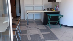 A compact kitchen with a built-in stove, a sink, and cabinets. There is a small dining table with chairs, a green folding table, and a patterned rug on the floor.