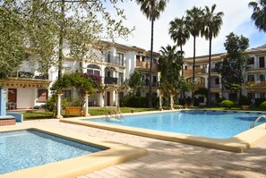A hotel with a swimming pool, palm trees, and a well-maintained garden.