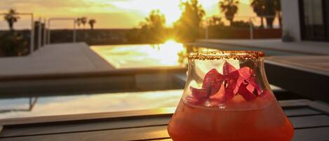 Ein Cocktail in einem Glas auf einem Holztisch, im Hintergrund ein Sonnenuntergang.