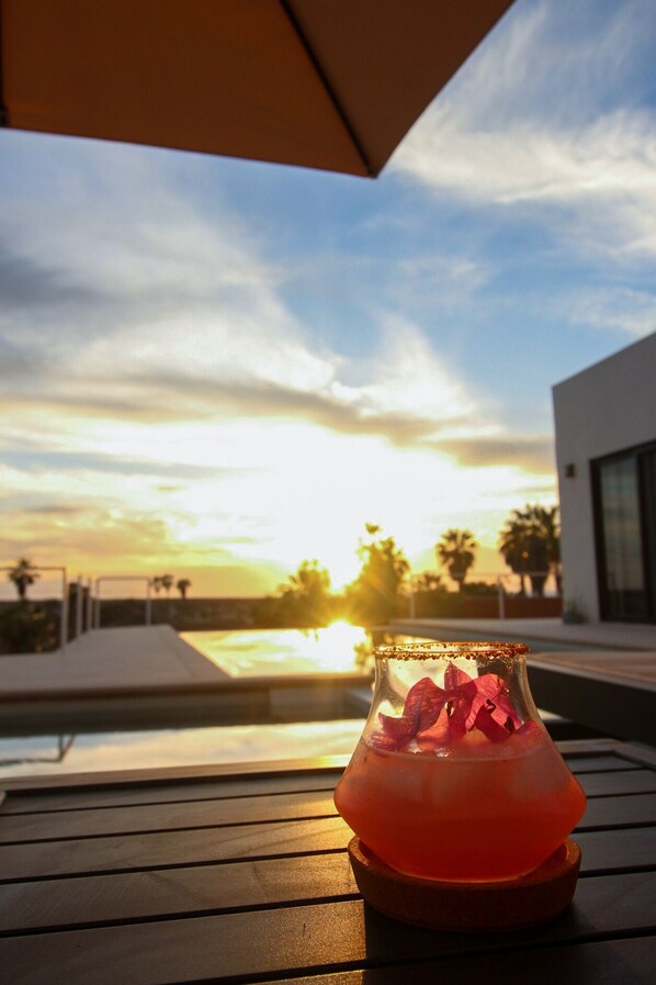 A cocktail in a glass on a wooden table with a sunset view in the background.