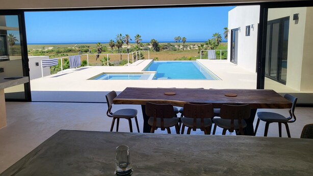 Un espace repas moderne offrant une vue sur une piscine et l’océan.