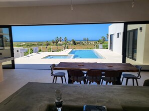 A modern dining area with a view of a swimming pool and the ocean.