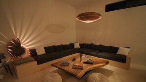 Un salon moderne avec un canapé d’angle aux lignes courbes, une table basse en bois et deux poufs ronds.