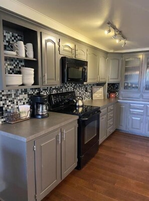 Kitchen features a black stove, stainless steel range hood, white cabinets, and a coffee maker.