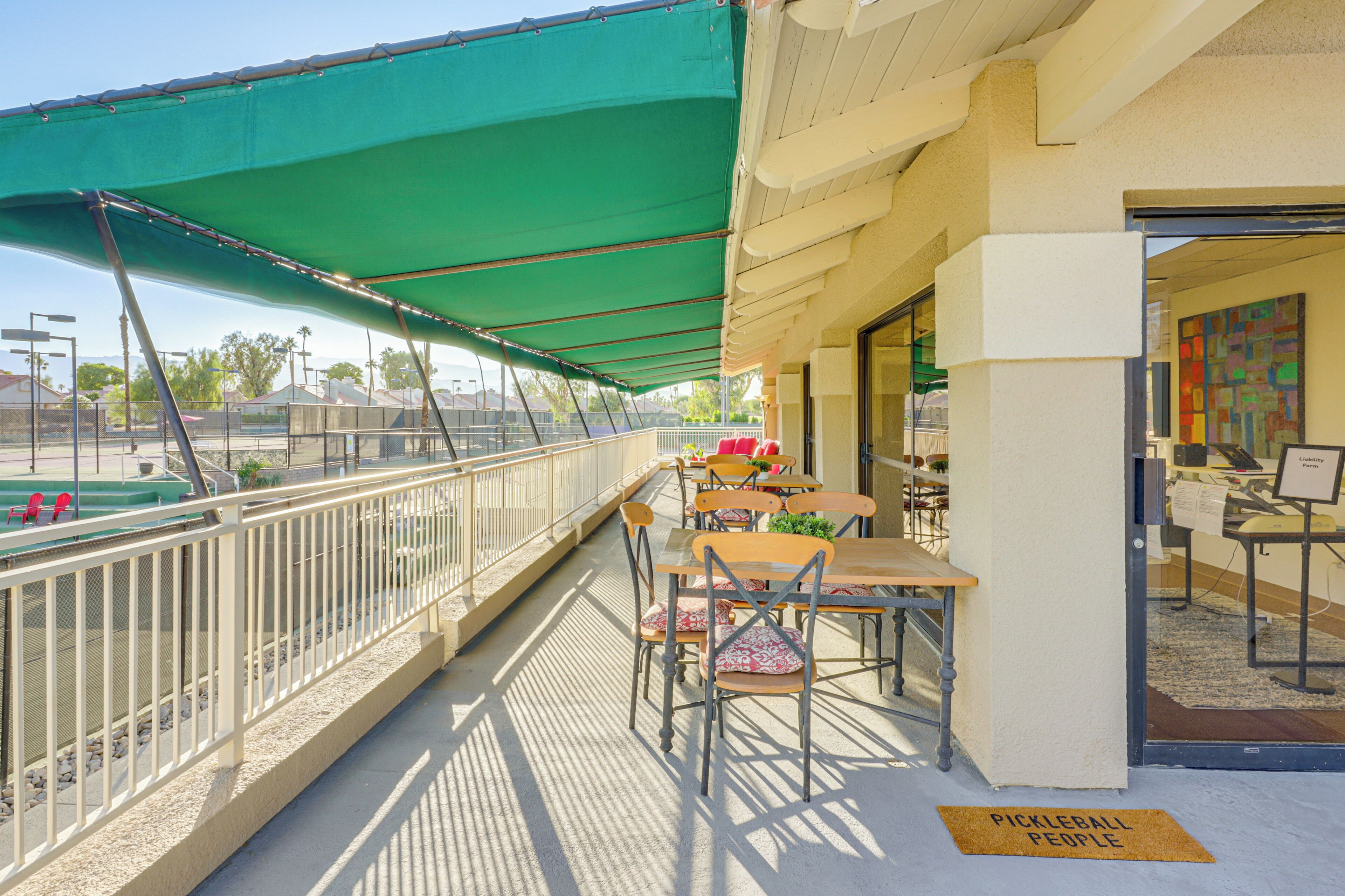 An outdoor seating area with tables and chairs, a green awning, and a sign that reads 'Pickleball People'.