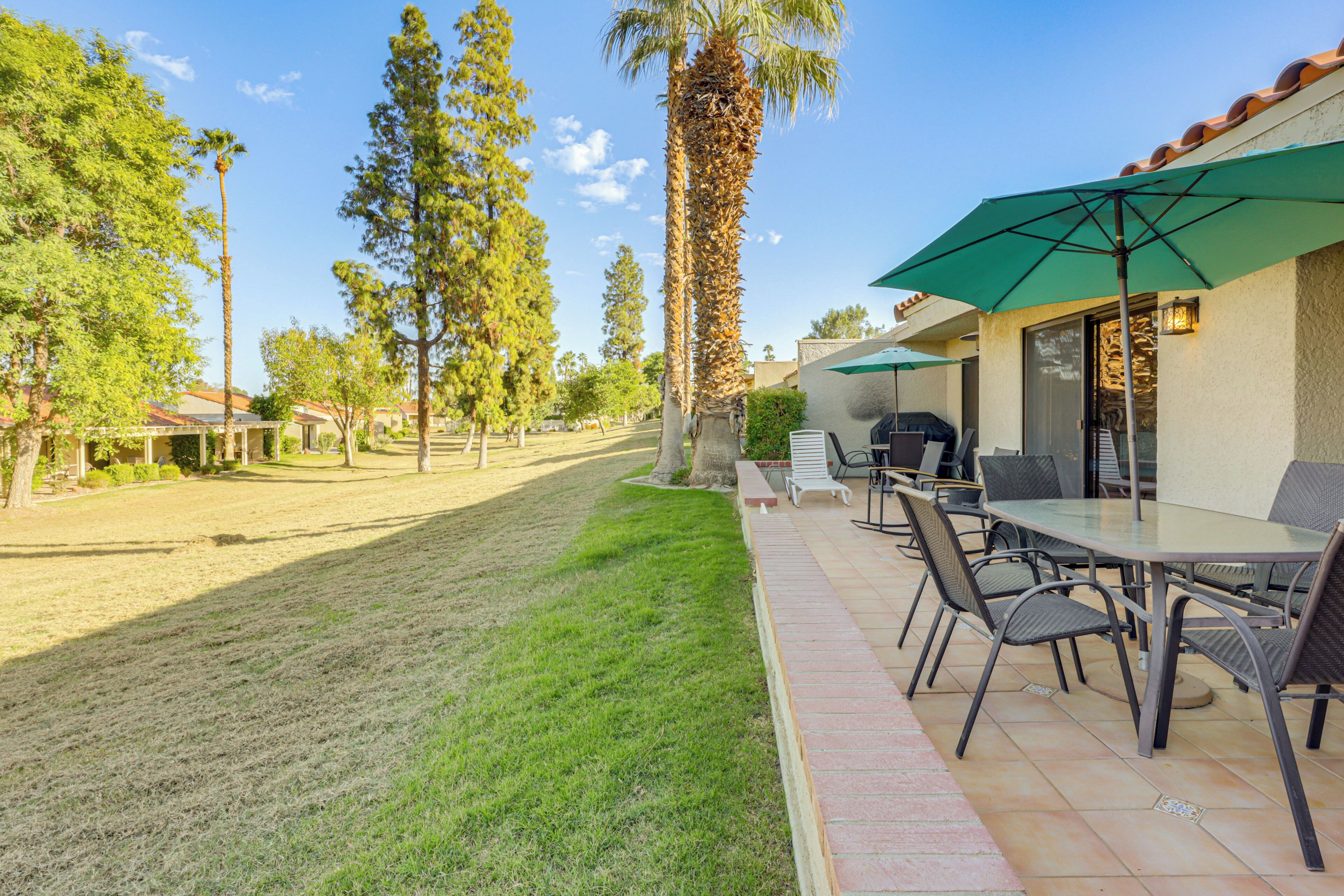 An outdoor patio area with a table and chairs, a green umbrella, and a barbecue grill.