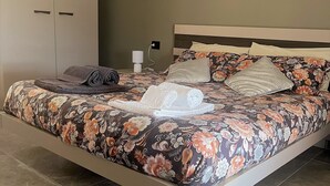A neatly made bed with floral bedding, a white headboard, and a painting on the wall.