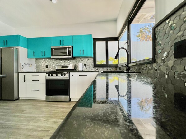 Una cocina moderna con armarios verde azulado, electrodomésticos de acero inoxidable y un ventanal grande.