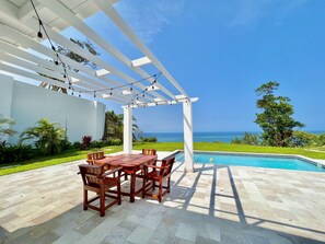 Un espace extérieur abrité, doté d’une piscine, de mobilier en bois et offrant une vue sur l’océan.