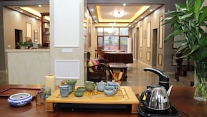 Un service à thé traditionnel posé sur un plateau en bois, une bouilloire électrique noire et un vase avec des plantes vertes dans le hall d’un hôtel.