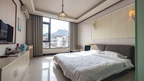 Une chambre d’hôtel équipée d’un lit, d’une télévision, d’un bureau avec une bouilloire, et offrant une vue sur les bâtiments à travers de grandes fenêtres.