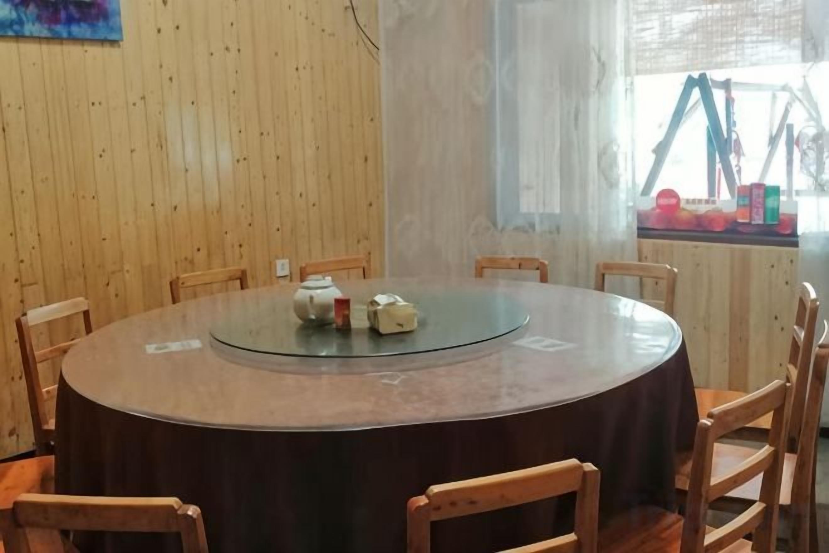 Une table ronde avec un plateau en verre, entourée de chaises en bois, placée devant un mur en bois orné d’une fenêtre.