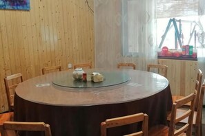 Una mesa redonda con superficie de vidrio rodeada de sillas de madera, frente a una pared de madera con una ventana.