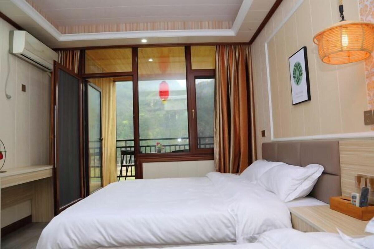 Ein Hotelzimmer mit Bett, Nachttisch, Fenster mit Vorhängen, Klimaanlage und Wandleuchte.