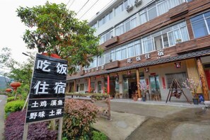 A hotel with a traditional Chinese architectural style, featuring a signboard with Chinese characters, a well-maintained garden with plants and a tree, and a clear view of the hotel's entrance. - Xianhua Farmhouse (Xianju)