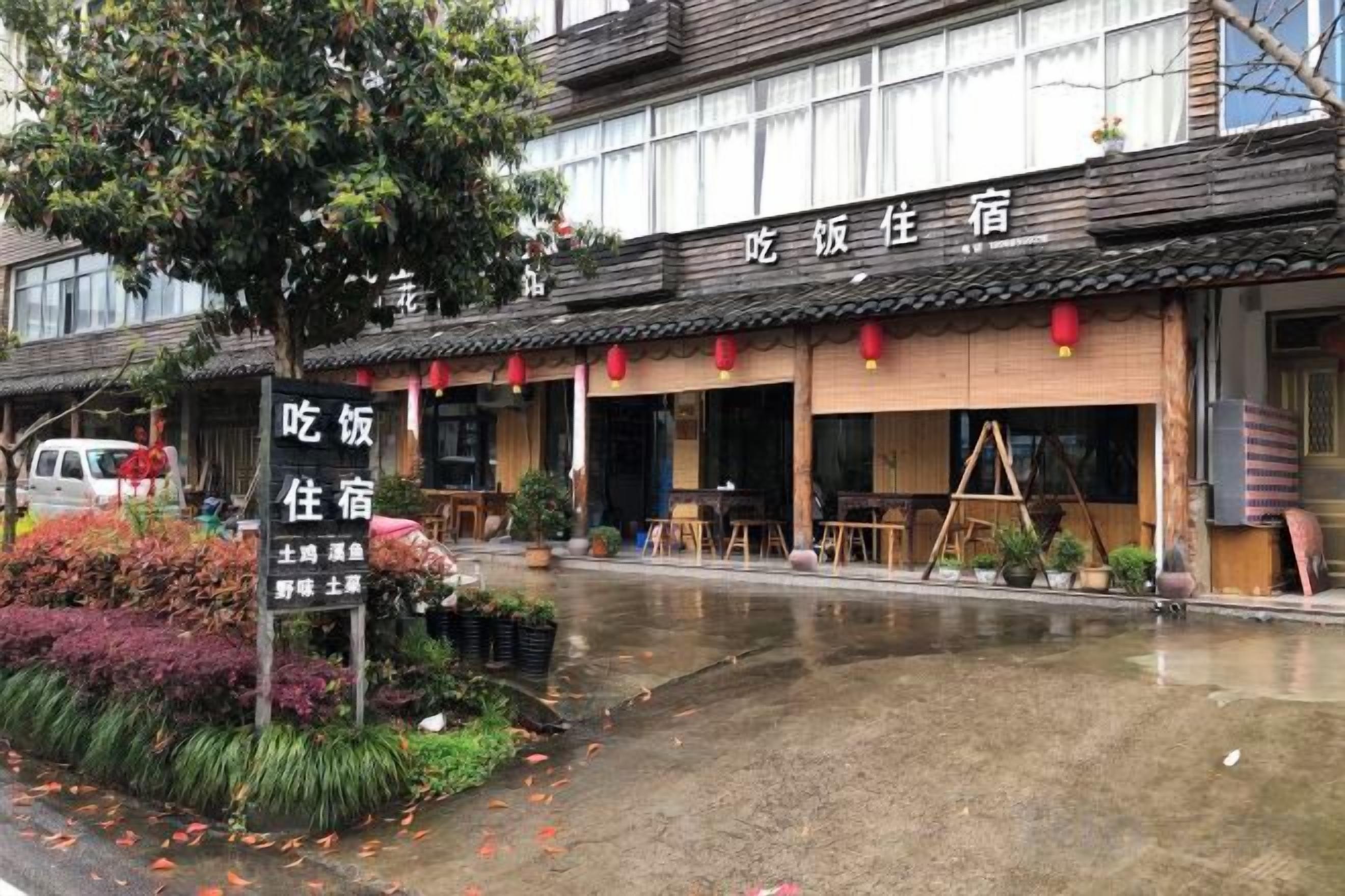A traditional building with a signboard, outdoor seating, and a wet ground, suggesting recent rain.