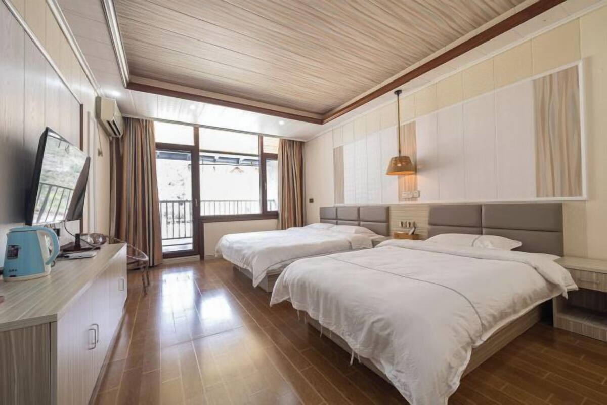 Ein Hotelzimmer mit zwei Betten, einem Fernseher, einer Kaffeemaschine und einem Balkon mit Vorhängen.