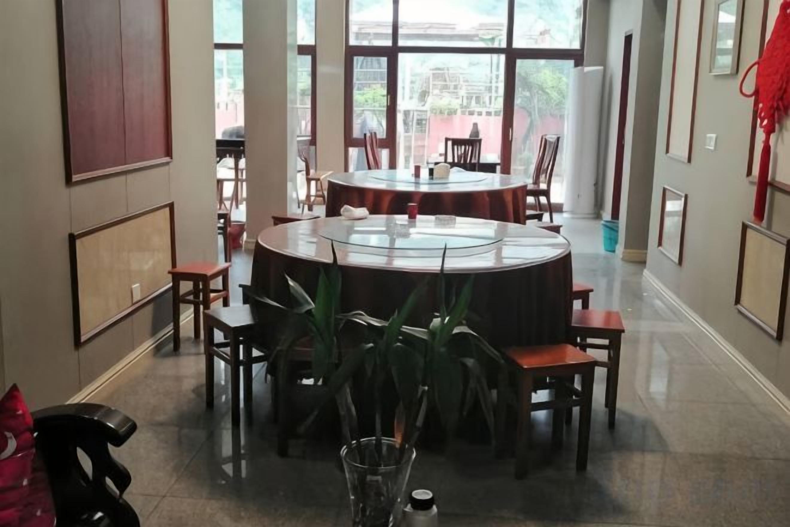 A dining area with a round table surrounded by chairs, large windows, and framed artwork on the walls.