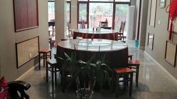 A dining area with a round table surrounded by chairs, large windows, and framed artwork on the walls.