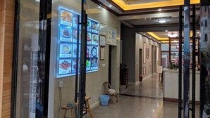 Un couloir avec un mur en verre sur lequel est affiché un menu, un comptoir d’accueil et une chaise.