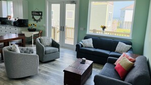 Un salon avec un canapé gris, deux fauteuils, une table basse et un coin repas comprenant une table et des chaises.