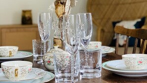 Une table à manger dressée avec de la vaisselle en verre transparent et des assiettes décorées de motifs floraux.
