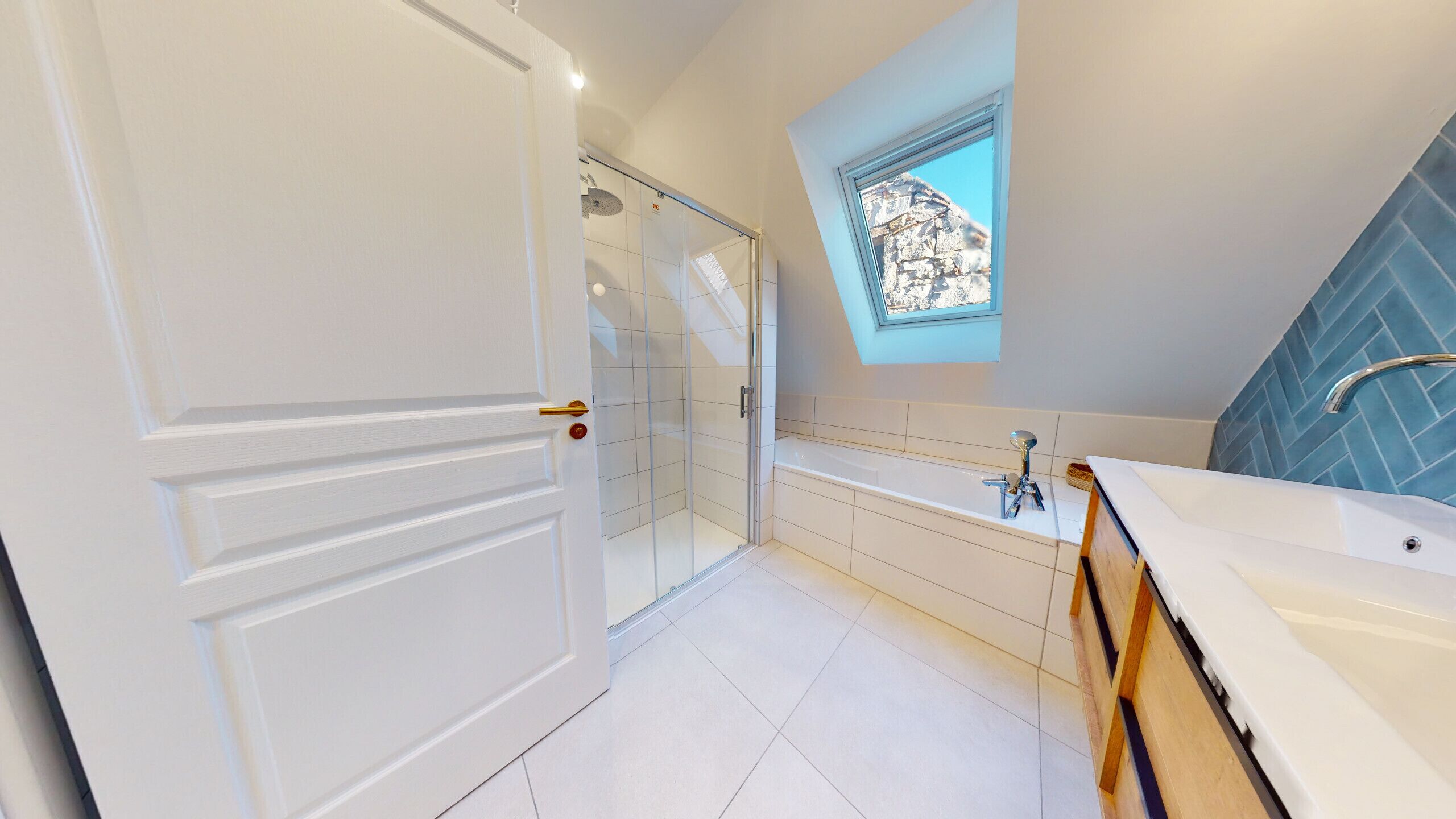 A modern bathroom with a glass shower enclosure, a freestanding bathtub, and a window with a stone wall view.