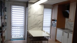 Une cuisine moderne avec un revêtement mural en marbre, un coin repas avec une table et des chaises blanches, et un plancher en bois.