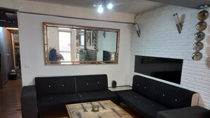 Un salon moderne avec un canapé d’angle noir, une commode en bois et un grand miroir au mur.
